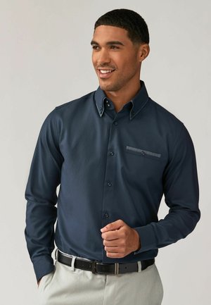 Marineblaues Hemd mit Knopfverschluss und strukturiertem Finish, ausgestattet mit einer Klappentasche und kontrastierenden Akzenten am Kragen und am Taschenrand.