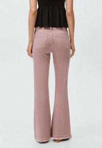 Flarede rosa jeans, tillverkade av mjukt bomull, har klassiska bakfickor och subtila sömnadsdetaljer. Avslutade fållar ger struktur.