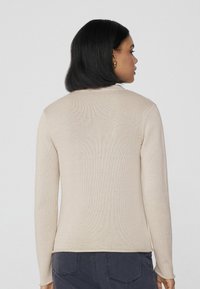 Suéter de punto beige con mangas largas, tejido texturizado, diseño ajustado y cuello redondo, mostrado desde la parte posterior.