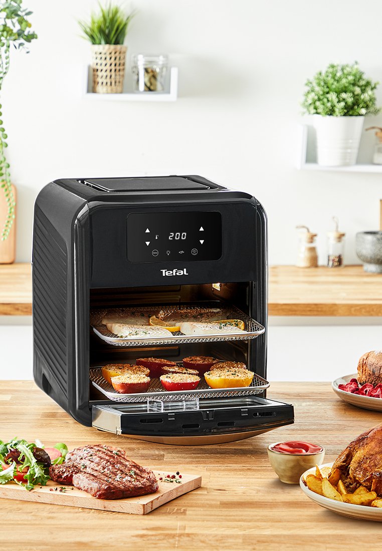 Tefal Heißluftfritteuse in Schwarz mit digitalem Bedienfeld. Zeigt drei Metallregale mit verschiedenen Lebensmitteln, darunter Gemüse und Fleisch.
