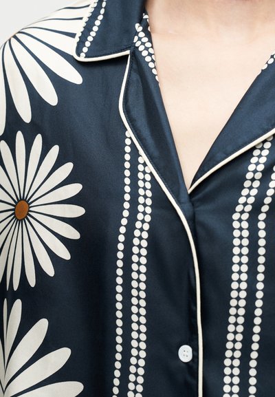 Μπλε ναυτικό σατέν πουκάμισο με σχέδια από λευκά μαργαριτάρια και διακεκομμένες γραμμές, με λευκή ρίγα κατά μήκος του γιακά και της σειράς κουμπιών.