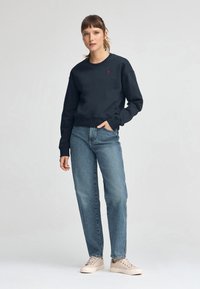 Marinblå bomullströja med rund halsringning och ribbade muddar, kombinerad med högmidjade ljusblå denimjeans och beige sneakers.