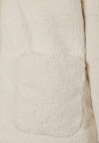 Artimas planas minkštos, grietinėlės spalvos dirbtinės kailio medžiagos, kurio paviršiuje prisisiūta kvadratinė kišenė.