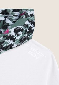 Indumento bianco con cappucci multi-colorati e a fantasia nei toni del verde, nero e accenni di rosa; logo “FREDDY MOV” in bianco.