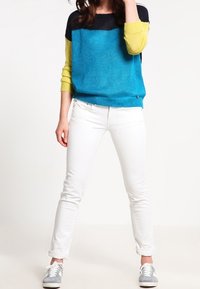 Färgglad pullover med en blå och svart överdel samt gula ärmar; kombinerad med vita slim-fit jeans och grå sneakers. Texturerat stickat tyg.