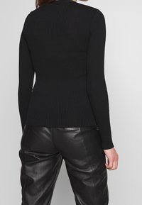 Maglietta nera a maniche lunghe con design aderente, caratterizzata da un collo rotondo e una texture sottile. Abbinata a pantaloni in pelle nera.
