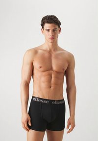 Cuecas boxer pretas feitas de algodão com ajuste justo. Apresentam uma cintura elástica com o logo "ellesse" em cinza. Textura lisa, sem padrões.