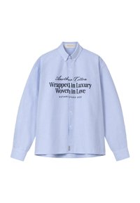 Camisa de manga larga a rayas en azul claro y blanco, con cuello y texto negro en el frente que dice "Otro algodón envuelto en lujo tejido con amor".