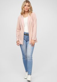 Lys pink blazer over en hvid skjorte, parret med lyseblå skinny jeans og hvide sneakers. Glat stof, skræddersyet pasform og minimalistiske detaljer.