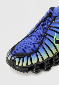 Sportsko med mesh-overside i blått og grønt gradient, svarte aksenter og karakteristisk såle som minner om en fjær. Har snøring og logodetalj.