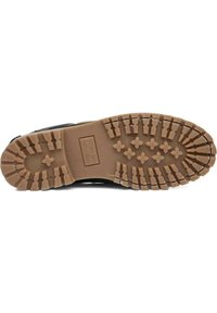 Suela de bota negra con un diseño texturizado y robusto. Presenta una suela de goma marrón con profundos surcos y una impresión de logo rectangular.