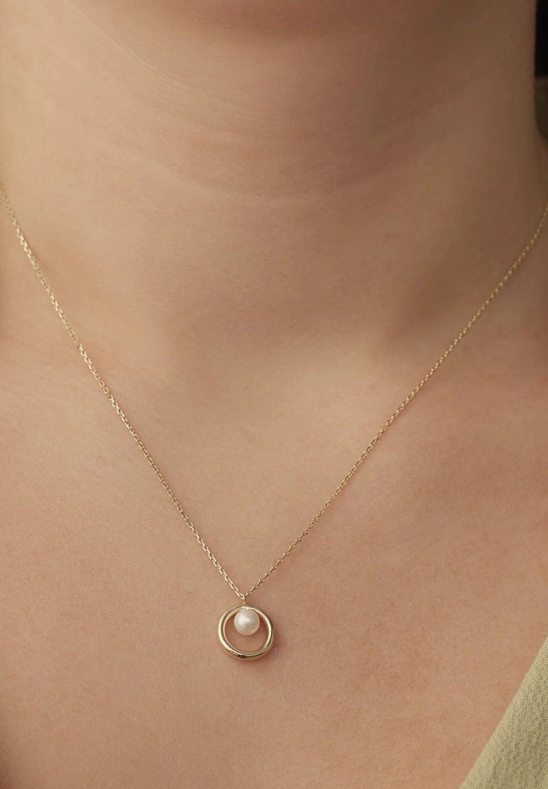 Goldkette mit einem runden Anhänger, der eine Perle in der Mitte zeigt, und einem glatten Textur sowie einem schlichten Design.