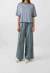 Pasiasty bawełniany t-shirt z krótkim rękawem w niebiesko-białe paski, zestawiony z szerokimi jasnoniebieskimi dżinsami o teksturowanym wykończeniu.