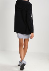 Felpa nera con cappuccio e strisce bianche, abbinata a una gonna grigia. La modella indossa scarpe da ginnastica grigie. Tessuto morbido.