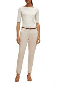 Gestreiftes, langärmliges Oberteil in Weiß und hellbeige; beiges Slim-Fit-Hose mit einem braunen Gürtel. Braune Slipper mit flachem Absatz.