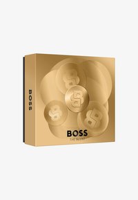 Scatola dorata con decorazioni circolari in rilievo e il logo "B". Il testo dice "BOSS THE SCENT" in nero. Superficie liscia, design moderno.