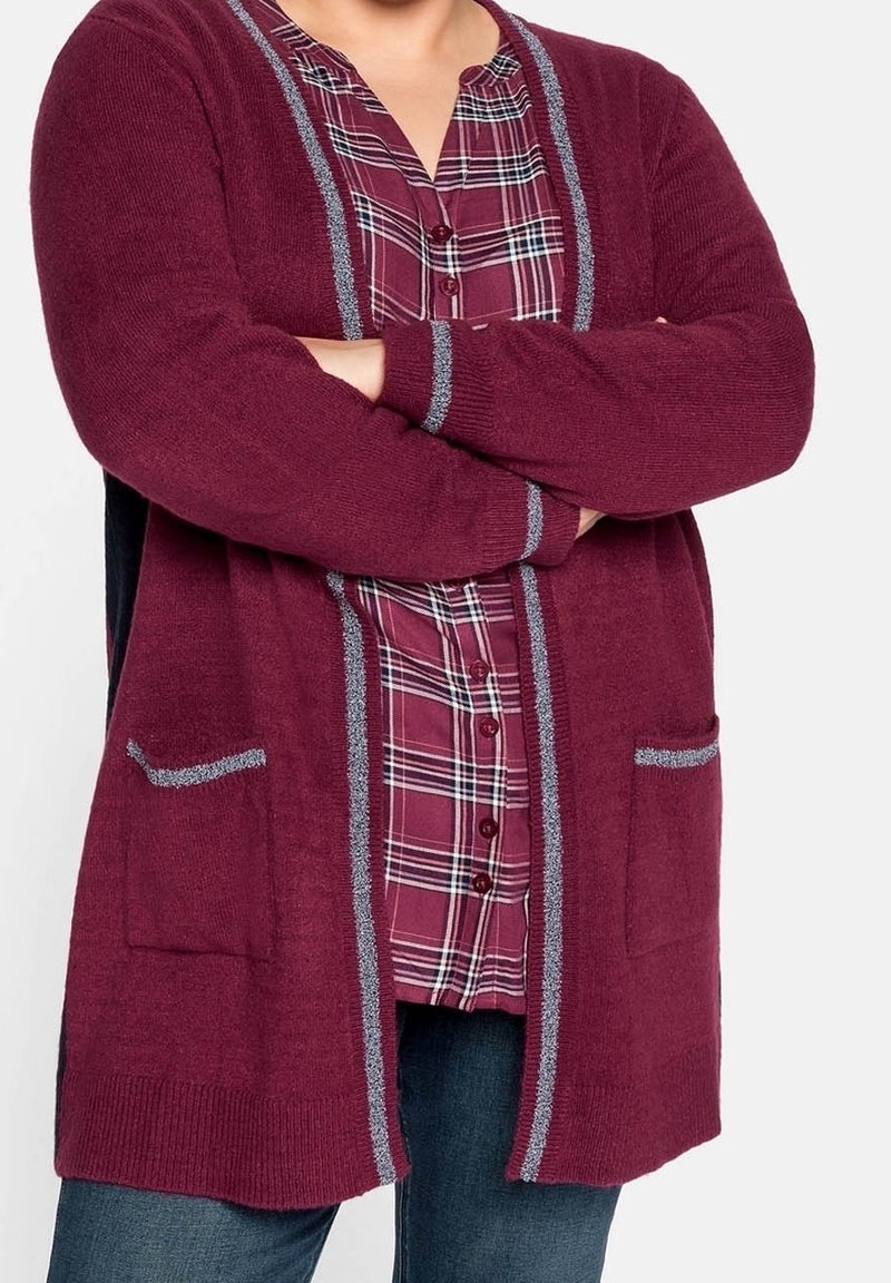 Cardigan bordeaux con accenti grigi, due tasche frontali, maniche lunghe e polsini a coste indossato sopra una camicia a quadri. Texture in maglia morbida.