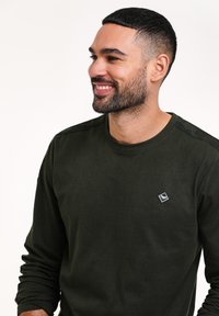T-shirt a maniche lunghe verde scuro realizzato in tessuto morbido, con una piccola patch del logo sul petto e dettagli sottili sulle spalle.