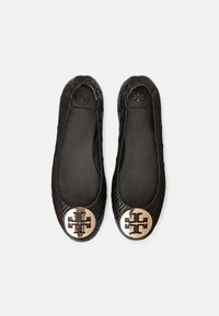 Ballerines en cuir noir avec une texture matelassée et un bout arrondi. Détail saisissant avec un logo doré sur le bout.