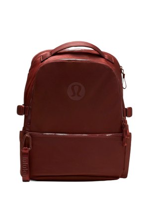 Kompaktný batoh tmavočervenej farby s horným držadlom, prednou zipsovou kapsou, bočnými nastavovacími popruhmi a diskrétnym kruhovým logom na prednom paneli.