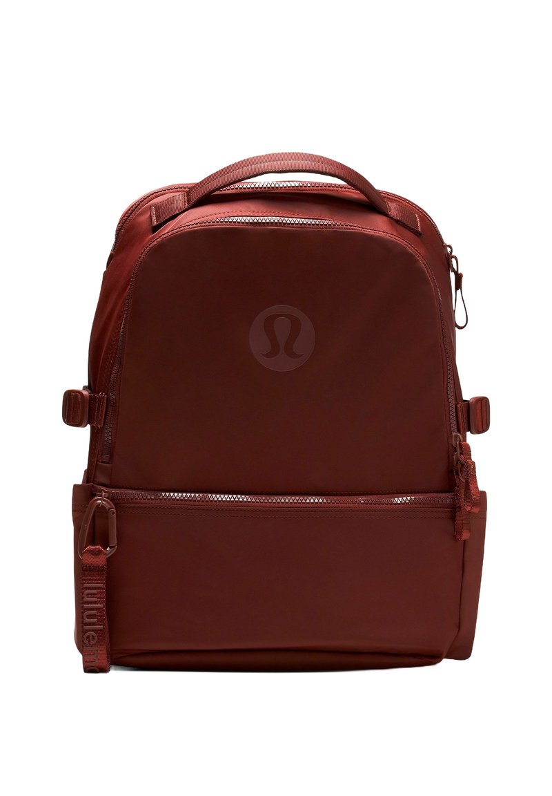 Kompakt sötétvörös hátizsák, felső fogantyúval, elülső cipzáras zsebbel, oldalsó állító pántokkal és diszkrét kör alakú logóval az elülső panelen.