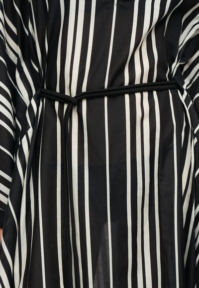 Vêtement à rayures verticales noires et blanches avec une fine ceinture noire tressée attachée autour de la taille.