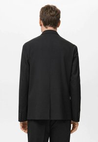 Giacca nera con design a schiena dritta. Presenta un colletto a risvolto e polsini con bottoni. Texture liscia, vestibilità su misura e stile minimalista.