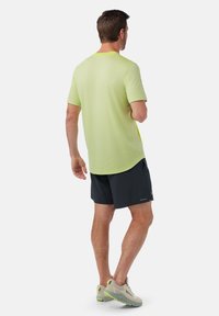 Lett, struktureret T-shirt med korte ærmer i klar neon-gul, parret med sorte shorts og letvægts løbesko i grå med gule detaljer.