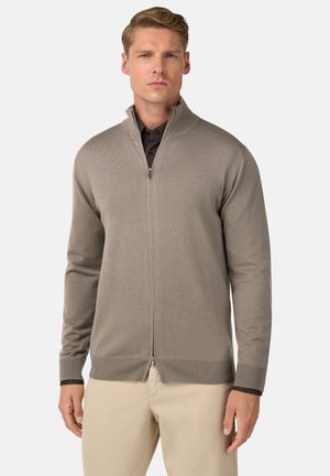 Beige Reißverschluss-Pullover mit strukturiertem Muster, gerippten Bündchen und Saum, kombiniert mit einem dunklen Hemd mit Kragen. Trägt ein Modell in einer neutralen Umgebung.