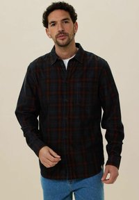 Zwarte en donkerrode geblokte flanellen shirt met een knoopsluiting aan de voorkant, lange mouwen en een borstzak, gecombineerd met lichtblauwe jeans.