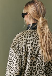 Manto di pelliccia con stampa leopardata e superficie morbida, in tonalità di crema e nero. Il colletto è nero, aggiungendo contrasto al design.