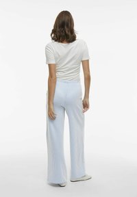 Witte top met korte mouwen gecombineerd met lichtblauwe wijde broek met verticale streepjes en elastische tailleband.