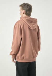 Rose-colored hoodie made from soft fabric, featuring a drawstring hood, long sleeves, and a relaxed fit. Plain design with no patterns.