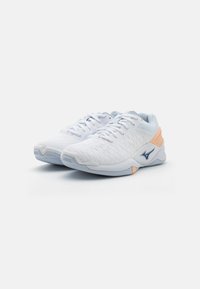 Baskets de sport blanches avec un dessus en mesh texturé, des accents bleu clair, un détail de talon orange et une semelle en caoutchouc durable. Design à lacets.
