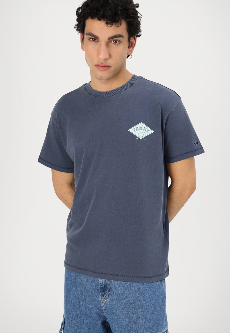 T-shirt en coton bleu marine avec un logo en diamant turquoise sur la poitrine et un col rond côtelé. Manches courtes, coupe décontractée.