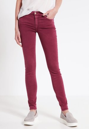 Burgundské skinny džíny vyrobené z bavlněného strečového materiálu, s hladkým povrchem, pěti kapsami a zapínáním na zip. V kombinaci se šedými slip-on botami.