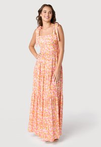 Robe maxi florale avec un décolleté carré, des bretelles réglables à nouer, une jupe à volants, dans des nuances de rose, orange et jaune sur un fond clair.