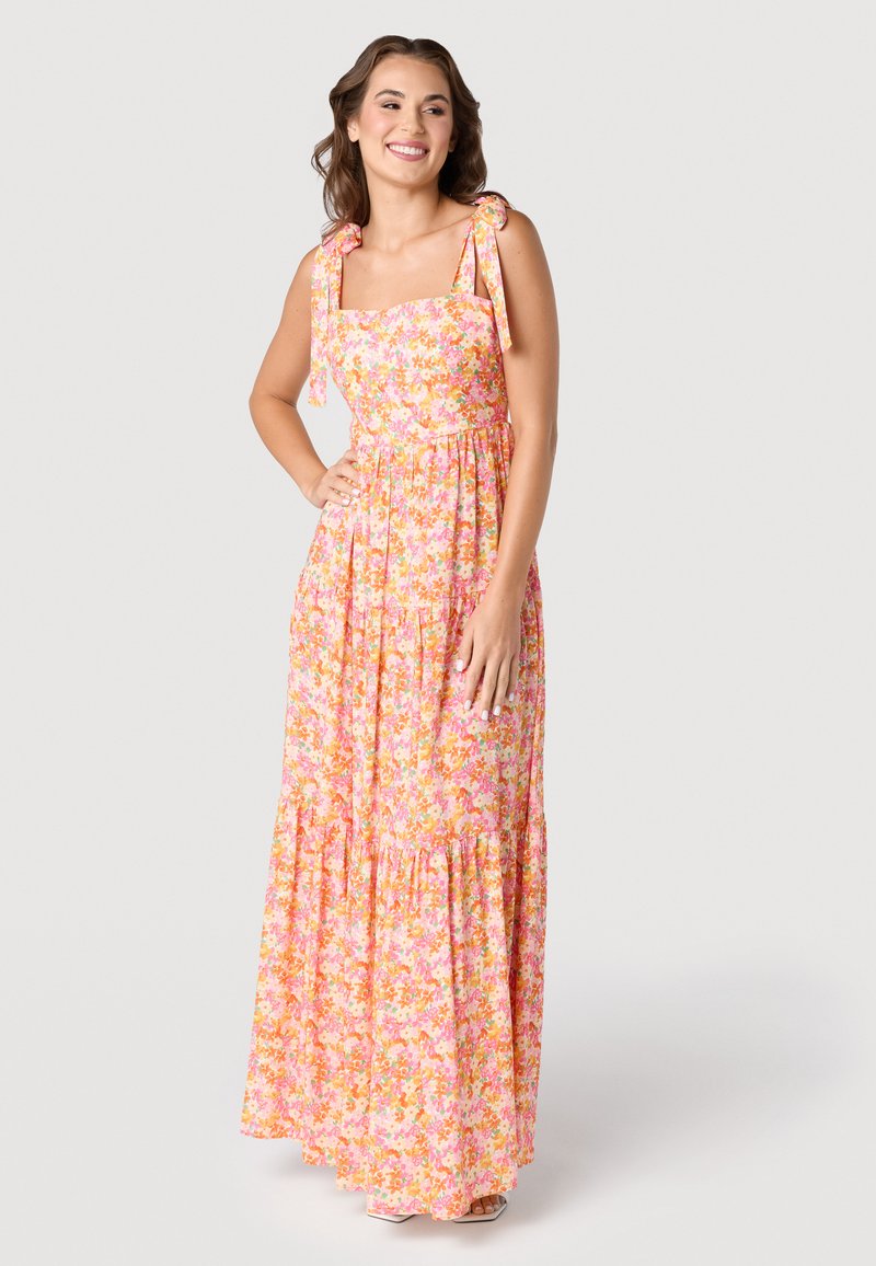 Robe maxi florale avec un décolleté carré, des bretelles réglables à nouer, une jupe à volants, dans des nuances de rose, orange et jaune sur un fond clair.
