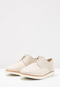 Chaussures beiges à lacets avec un dessus texturé, une finition lisse et une semelle en caoutchouc blanche. Présente des coutures discrètes et un design épuré.