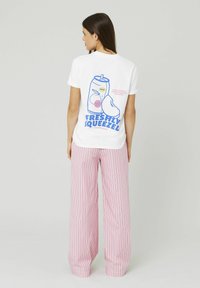 T-shirt en coton blanc avec un graphisme coloré au dos représentant une canette de limonade et du texte. Pantalons larges rayés roses et blancs.