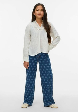 Camisa blanca de manga larga con textura, cuello y detalles de encaje, combinada con vaqueros azules con un patrón de corazones y un ajuste relajado.