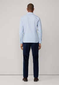 Camicia azzurro chiaro con maniche lunghe, colletto e yoke posteriore; abbinata a pantaloni di velluto a coste blu navy e scarpe marroni.