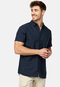 Camisa de manga corta de color navy hecha de tela de algodón, con cuello abotonado, un bolsillo en el pecho y un dobladillo recto.