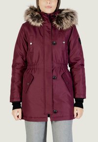 Giacca puffer bordeaux con cappuccio in pelliccia sintetica, vita con coulisse, due tasche laterali e bottoni neri. Presenta polsini a coste e una texture liscia.