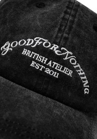 Cappello in denim nero con ricamo bianco della scritta "Good For Nothing," con "BRITISH ATELIER" e "EST 2011" sotto in un motivo ad arco.