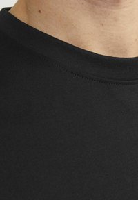 Camiseta negra de manga corta con una textura de algodón suave, un cuello redondo clásico y detalles de costura sutiles a lo largo del cuello.