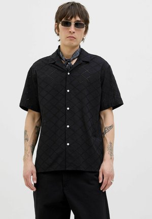 Black short-sleeve shirt with a diamond cut-out pattern, white buttons, and a collar. Worn with a black scarf and black pants.