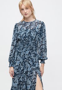 Ρουά αέρινο φόρεμα με μπλε πασλεϊν μοτίβο, μακριά φουσκωτά μανίκια, ελαστική μέση και πλαϊνή σχισμή, κατασκευασμένο από ελαφρύ ύφασμα.