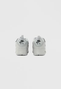 Szürke Nike Air edzőcipők texturált felsőrésszel, kerekded formával, sarkon húzófülekkel és fekete logó díszítéssel a hátoldalukon.