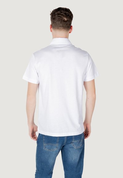 T-shirt en coton blanc avec un col classique et des manches courtes, vue de l'arrière. Associé à un jean en denim bleu. Design épuré sans motifs.
